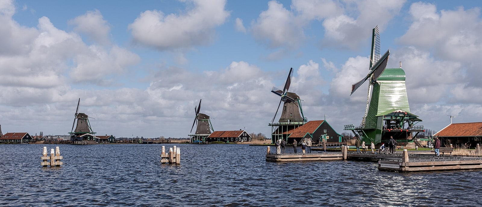 The windmills of Zaanse Schans lined up beside the water, under a cloudy sky