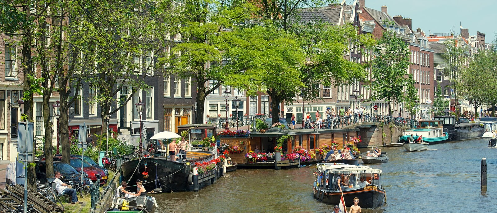 Un canal del Jordaan con casas flotantes, árboles y gente sentada en la orilla