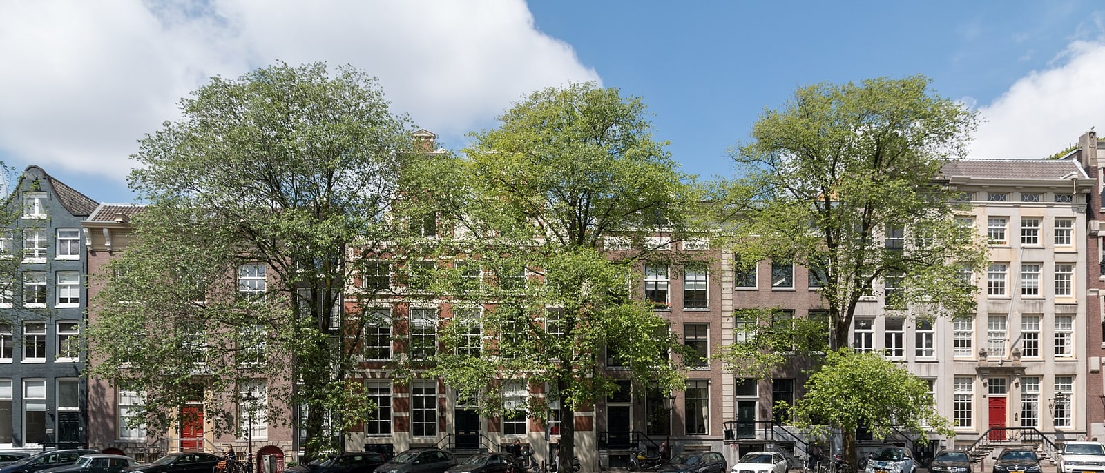 A row of canal houses with trees in front and bicycles parked along the street
