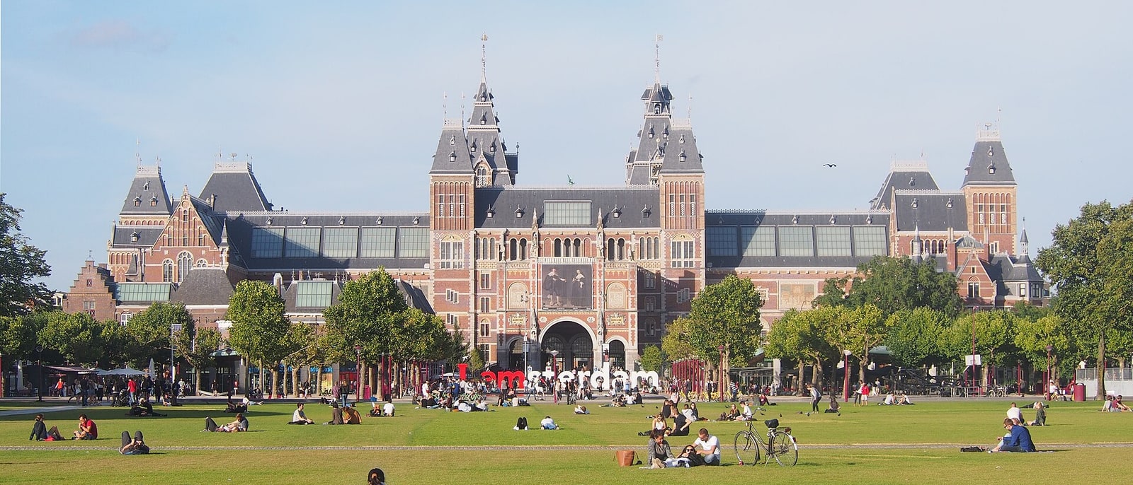 The Rijksmuseum seen across the Museumplein lawn, people sitting on the grass