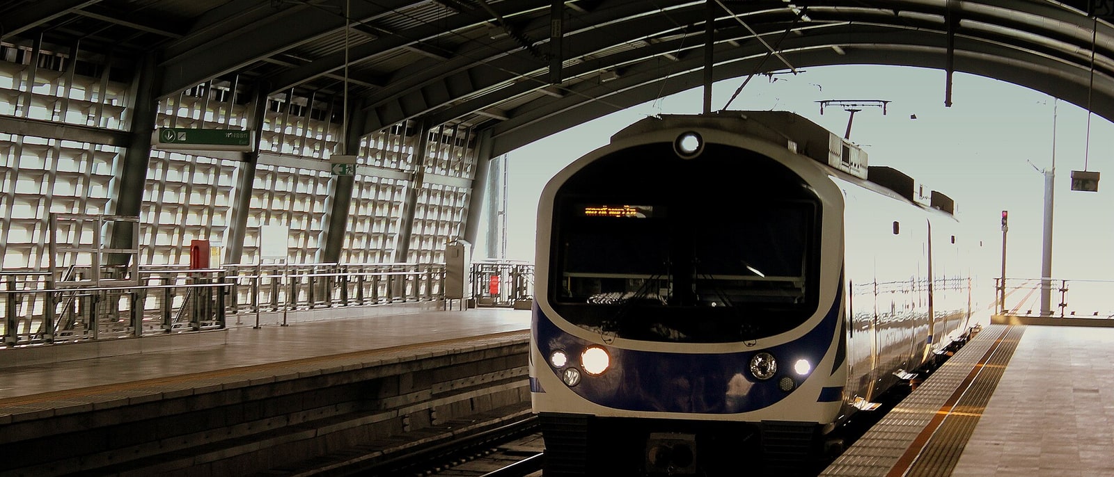 An Airport Rail Link train pulling into an elevated station, backlit