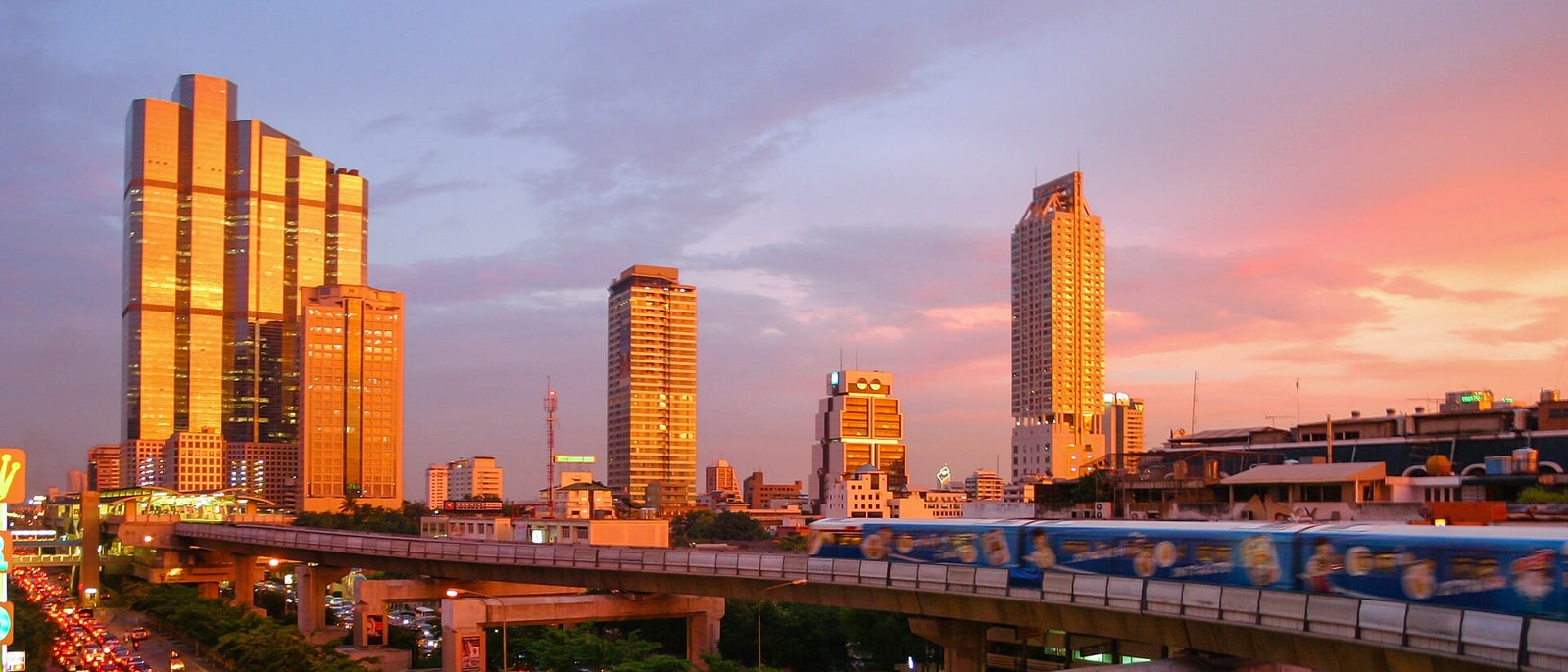 The Skytrain gliding along its viaduct at dusk, above the jammed avenue below