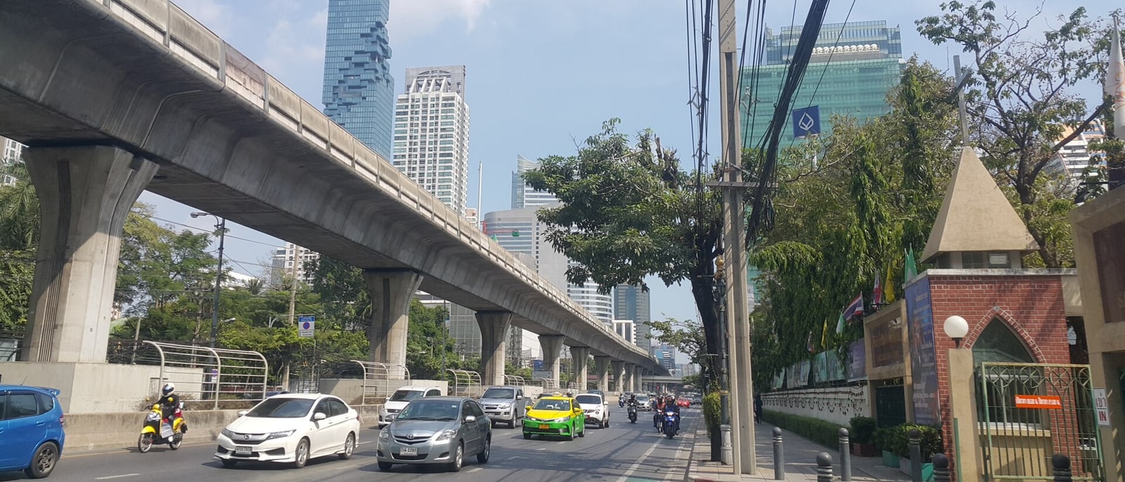 The Skytrain viaduct over the Sathon Tai traffic in full sun, cables and towers behind