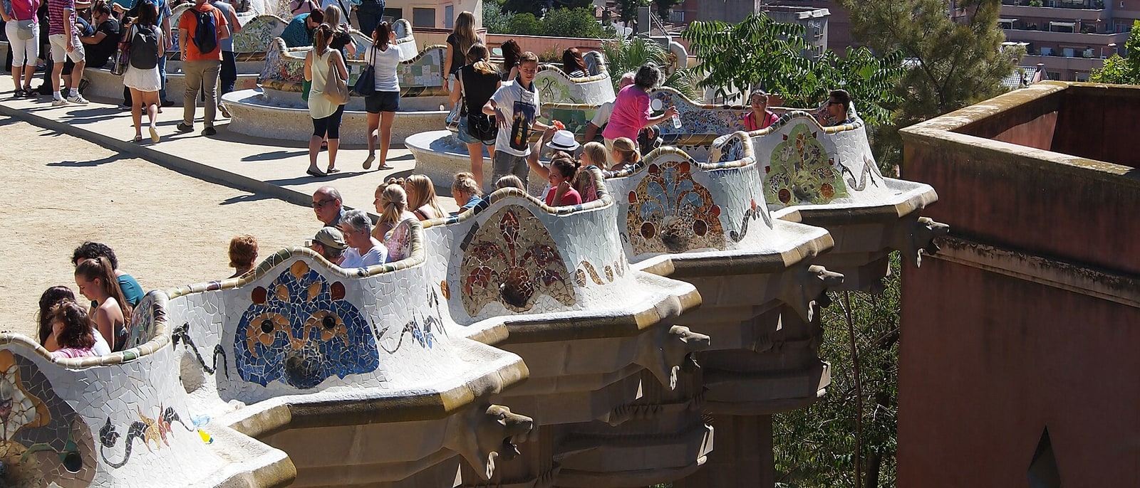 Park Güell’s mosaic bench crowded with people, the city and sea beyond
