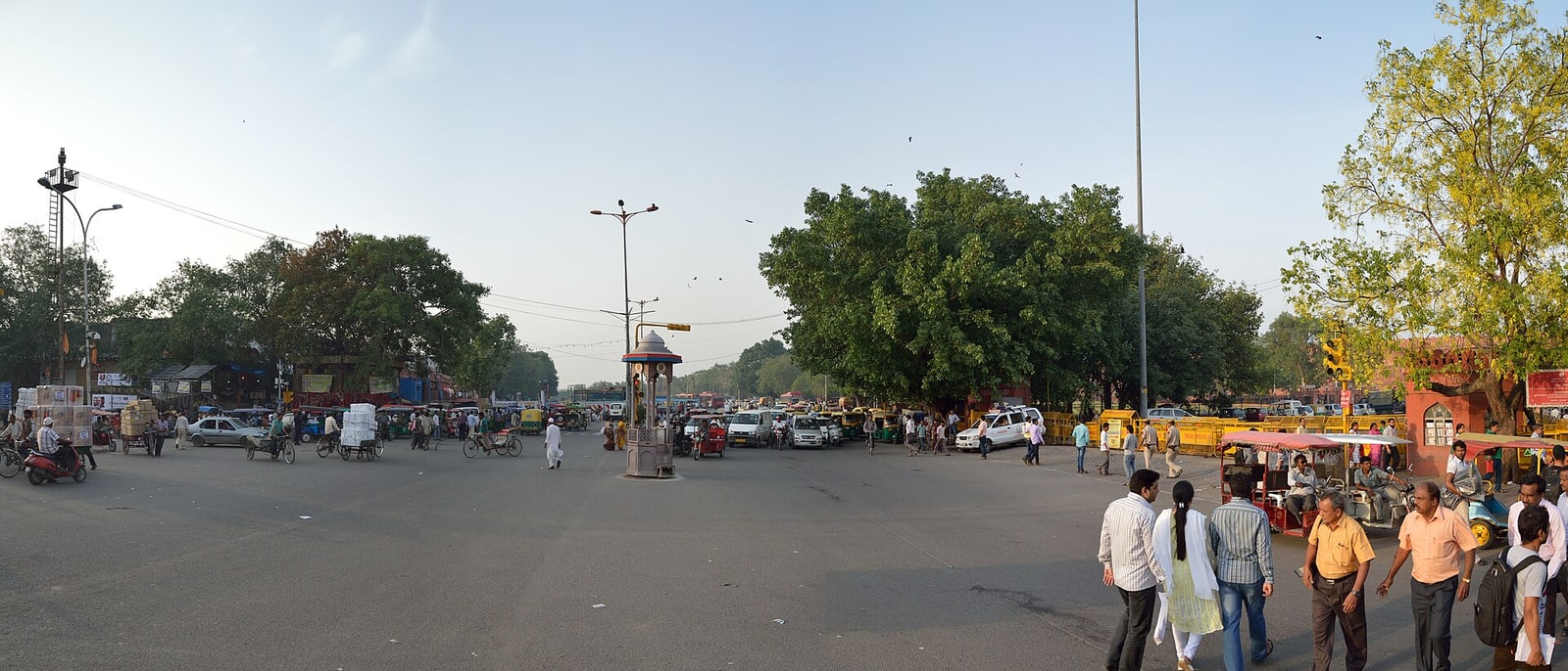 A wide junction in Old Delhi with traffic and people crossing