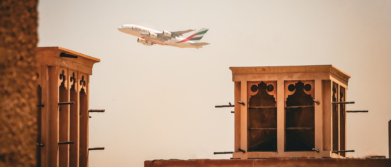The wind towers of Al Fahidi with an Emirates aircraft passing overhead