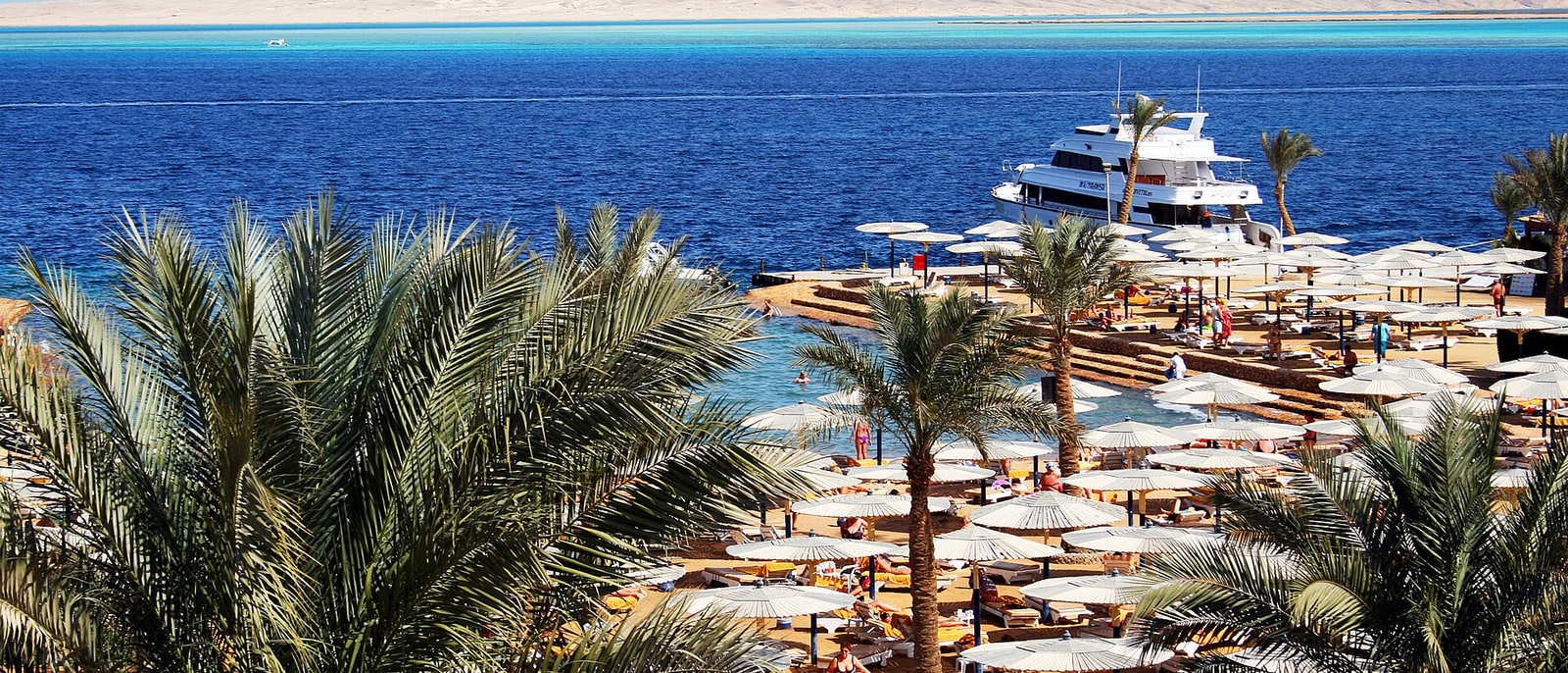 La playa de un hotel de Hurgada con las sombrillas y los yates amarrados detrás