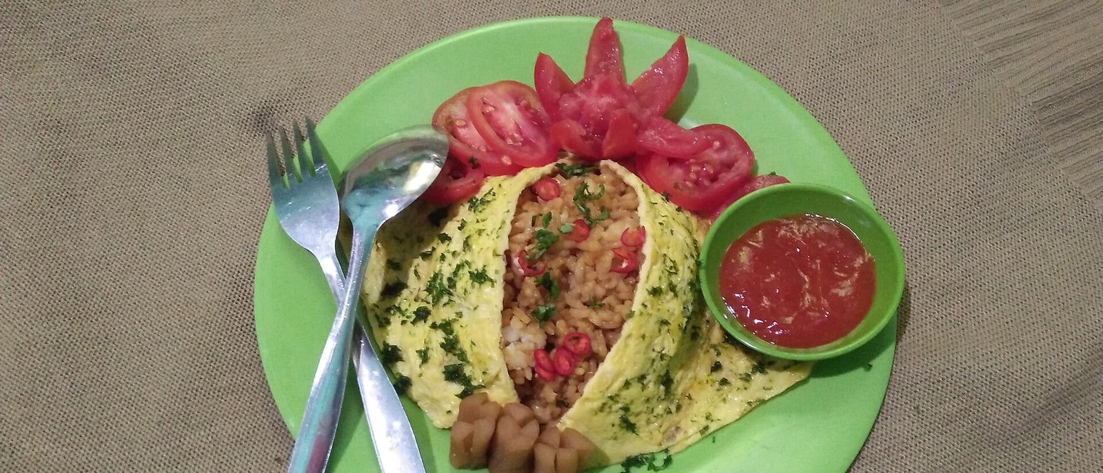 Nasi goreng wrapped in omelette, with garnish and sambal