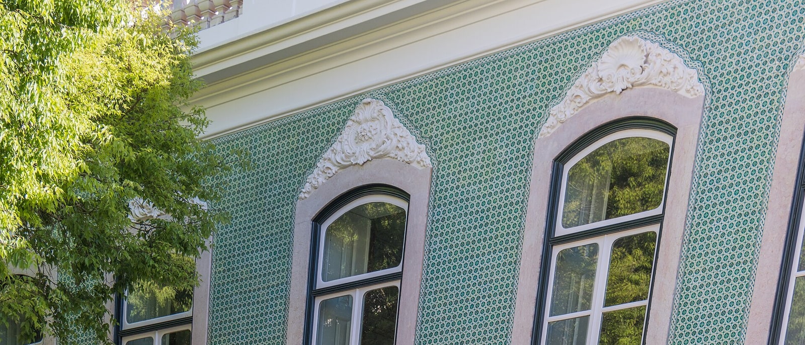 A Lisbon façade covered in green azulejos, its windows framed in white