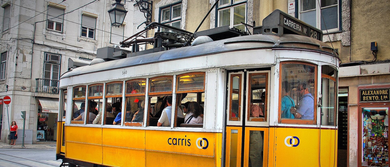 A yellow Carris tram, one of the old ones, in a narrow street
