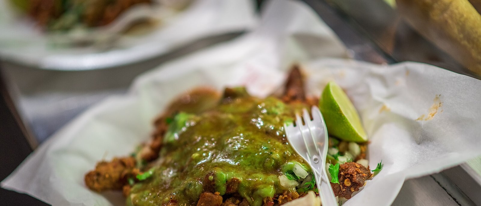 Un taco con salsa verde y una rodaja de lima, servido en papel
