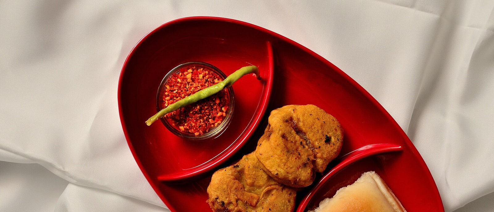 A vada pav served on a red plate, with its chilli