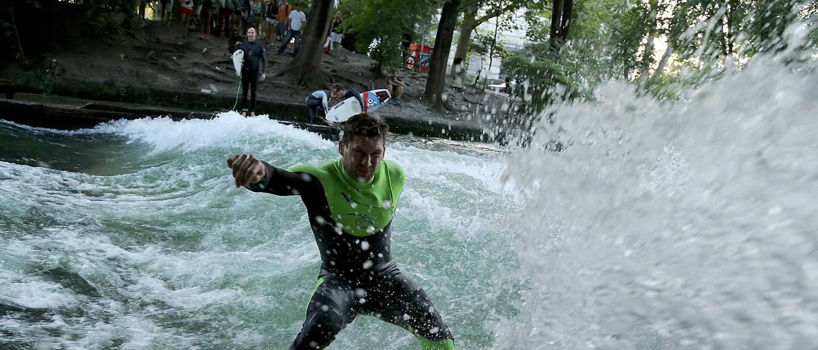 A surfer on the Eisbach standing wave, the queue waiting their turn on the bank behind