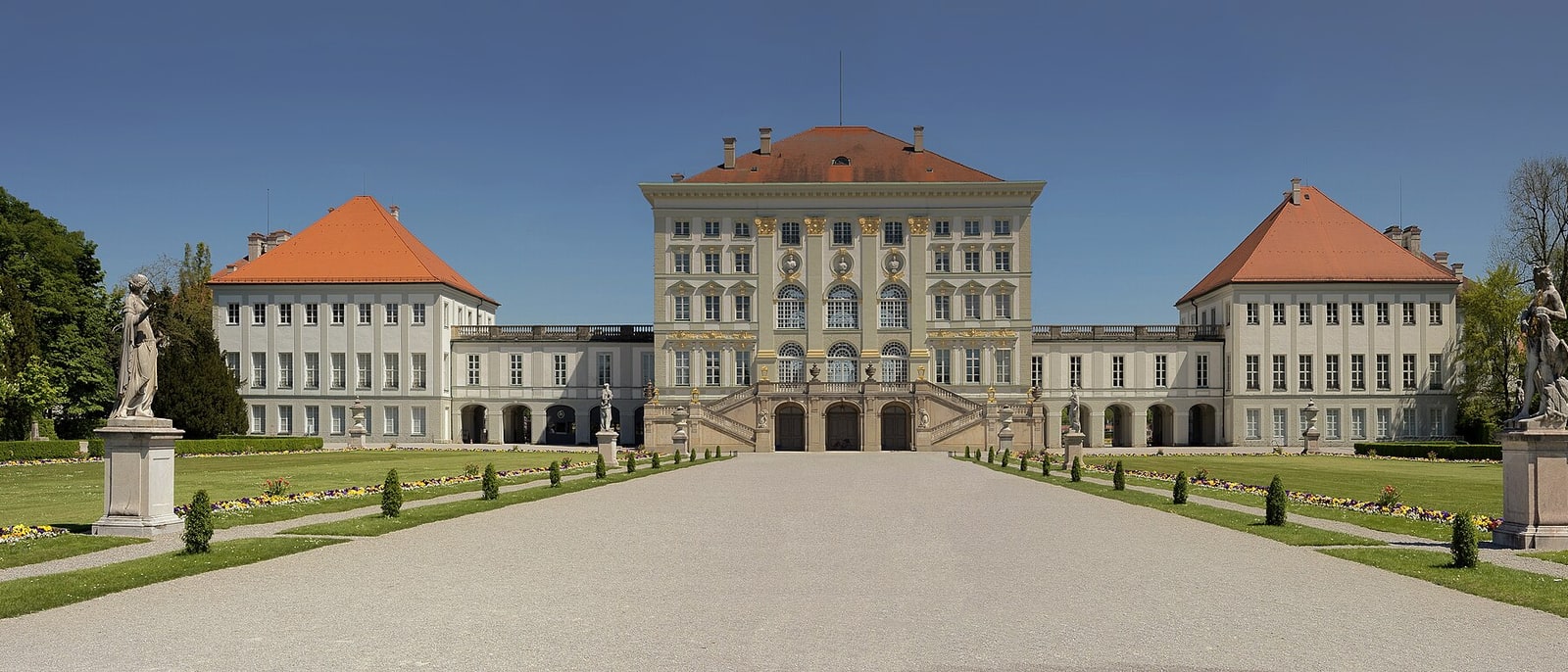 Nymphenburg’s baroque facade head-on from the gravel avenue, statues flanking it