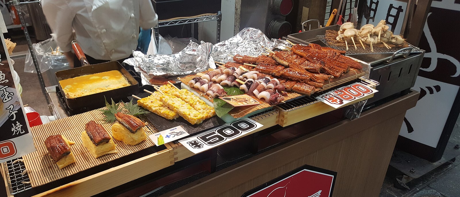 A prepared-food counter with skewers and omelette, prices displayed