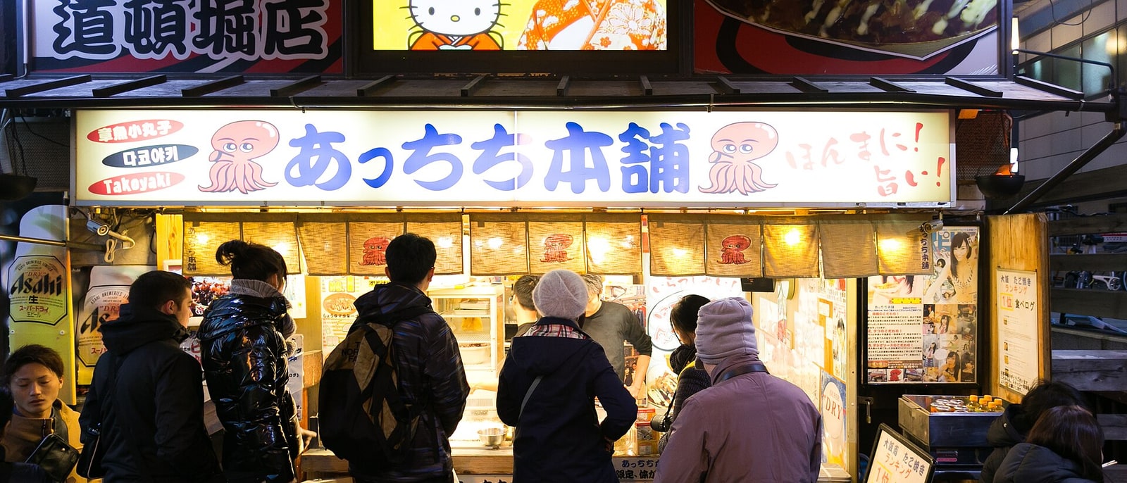 A takoyaki stall in Dotonbori with people waiting at the counter