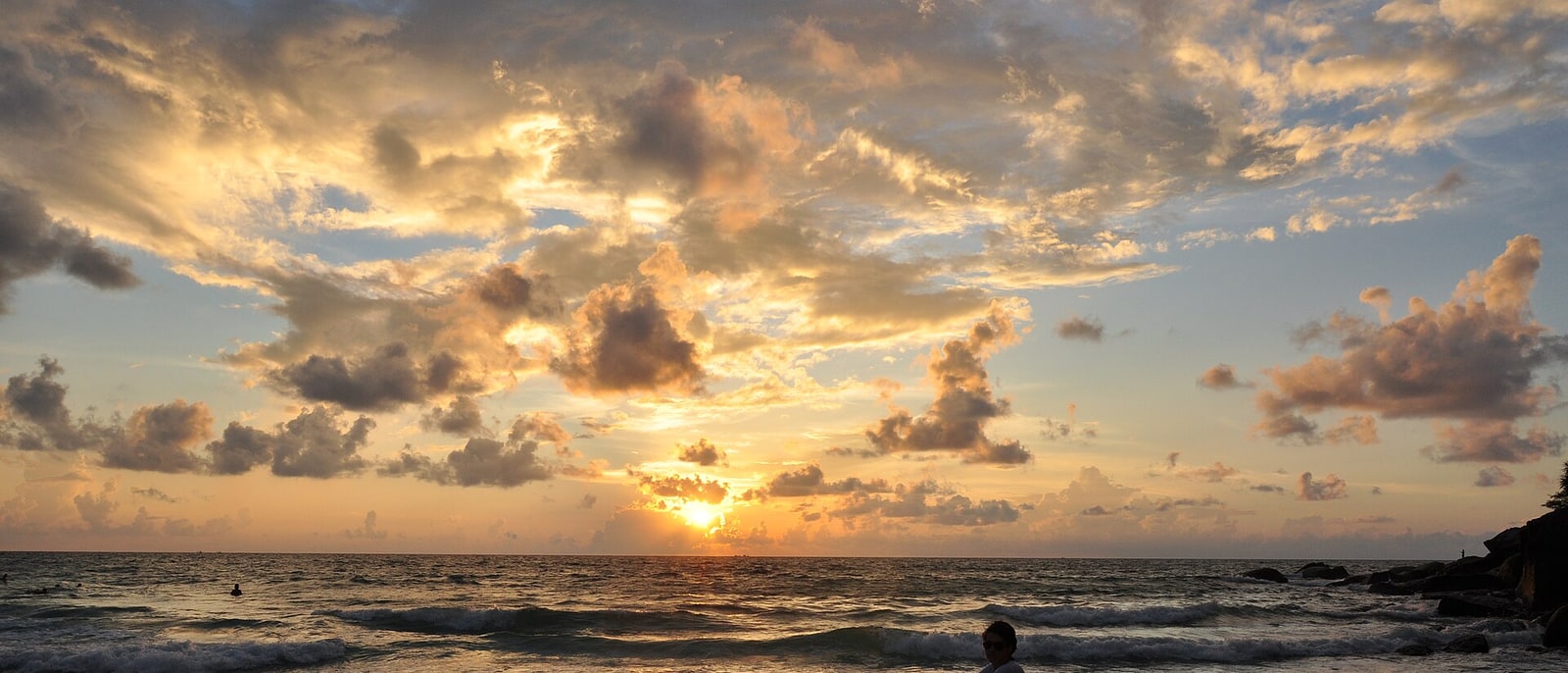 Kata Noi at dusk: the sun dropping into the Andaman Sea, a rock on the shoreline