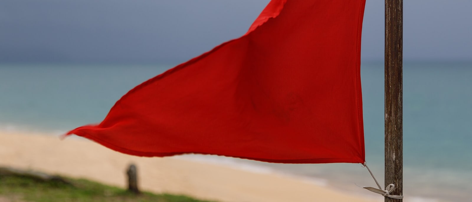 The red warning flag snapping on Mai Khao beach, overcast sky behind