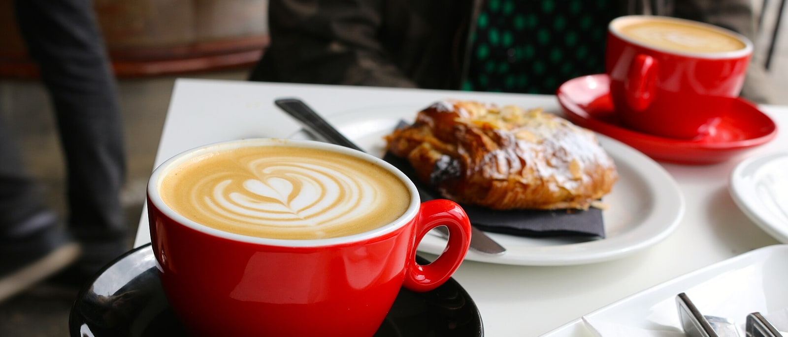 Two flat whites in red cups with a croissant, in a café