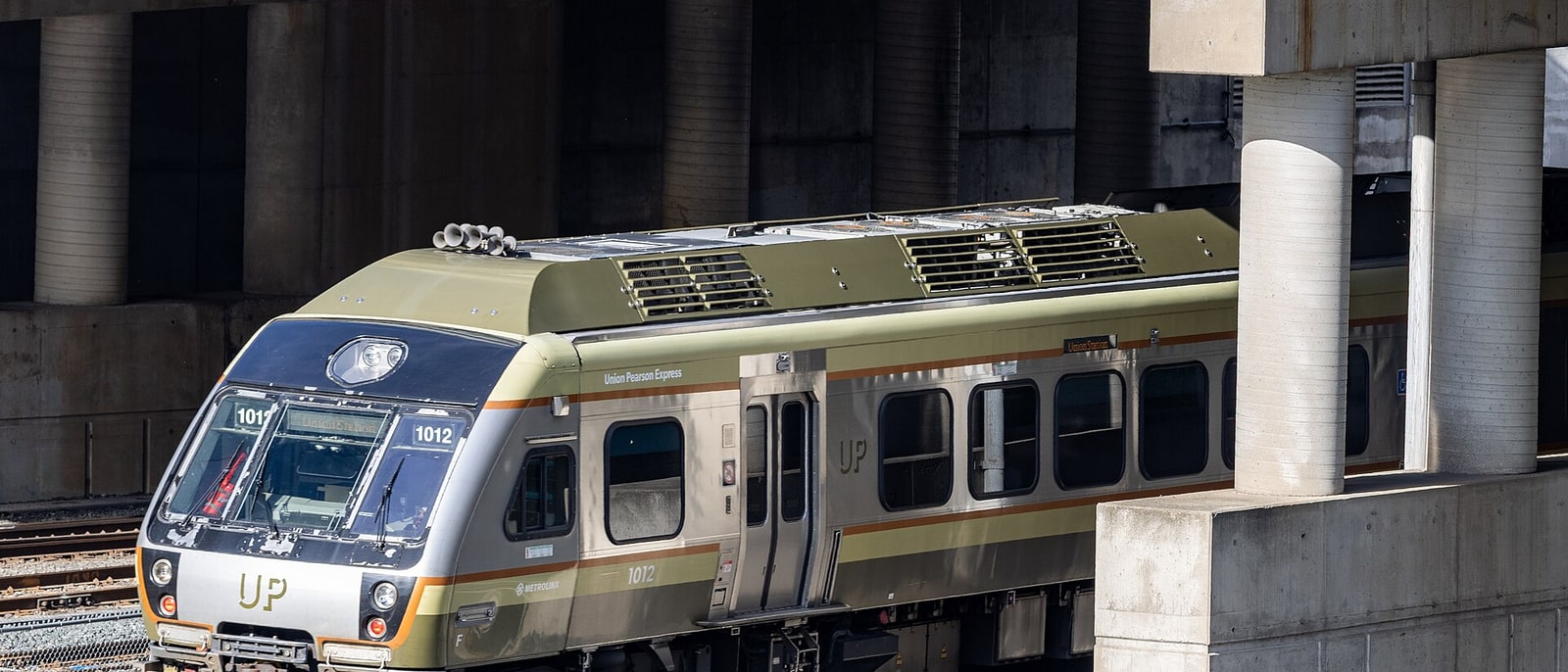 Un tren del UP Express, con su librea verde y crema, parado bajo la estructura de la estación