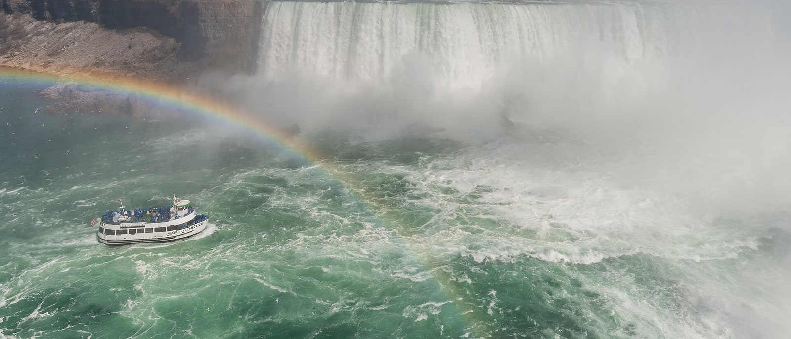 Un barco acercándose al pie de las cataratas del Niágara, con un arcoíris en la nube de agua