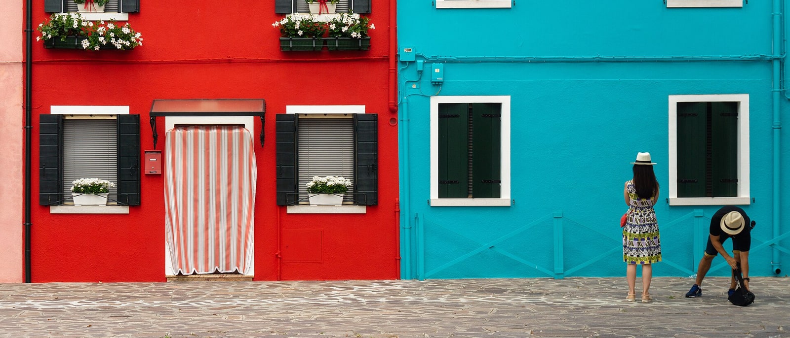 Two Burano houses, one red and one turquoise, people in front